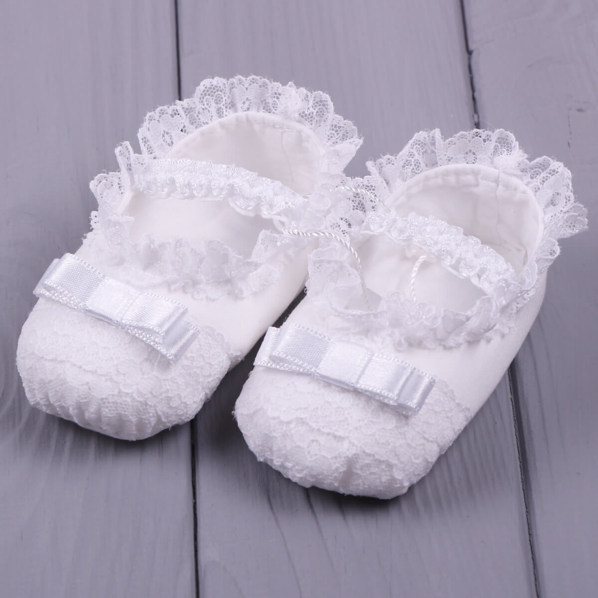 Christening Booties  with lace details on a gray wooden surface