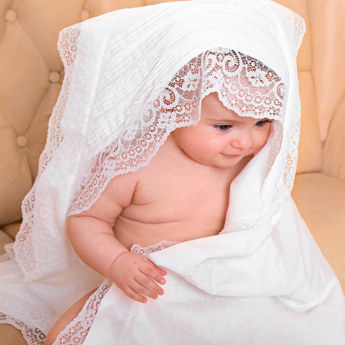 Baby wrapped in a white lace blanket on a beige couch