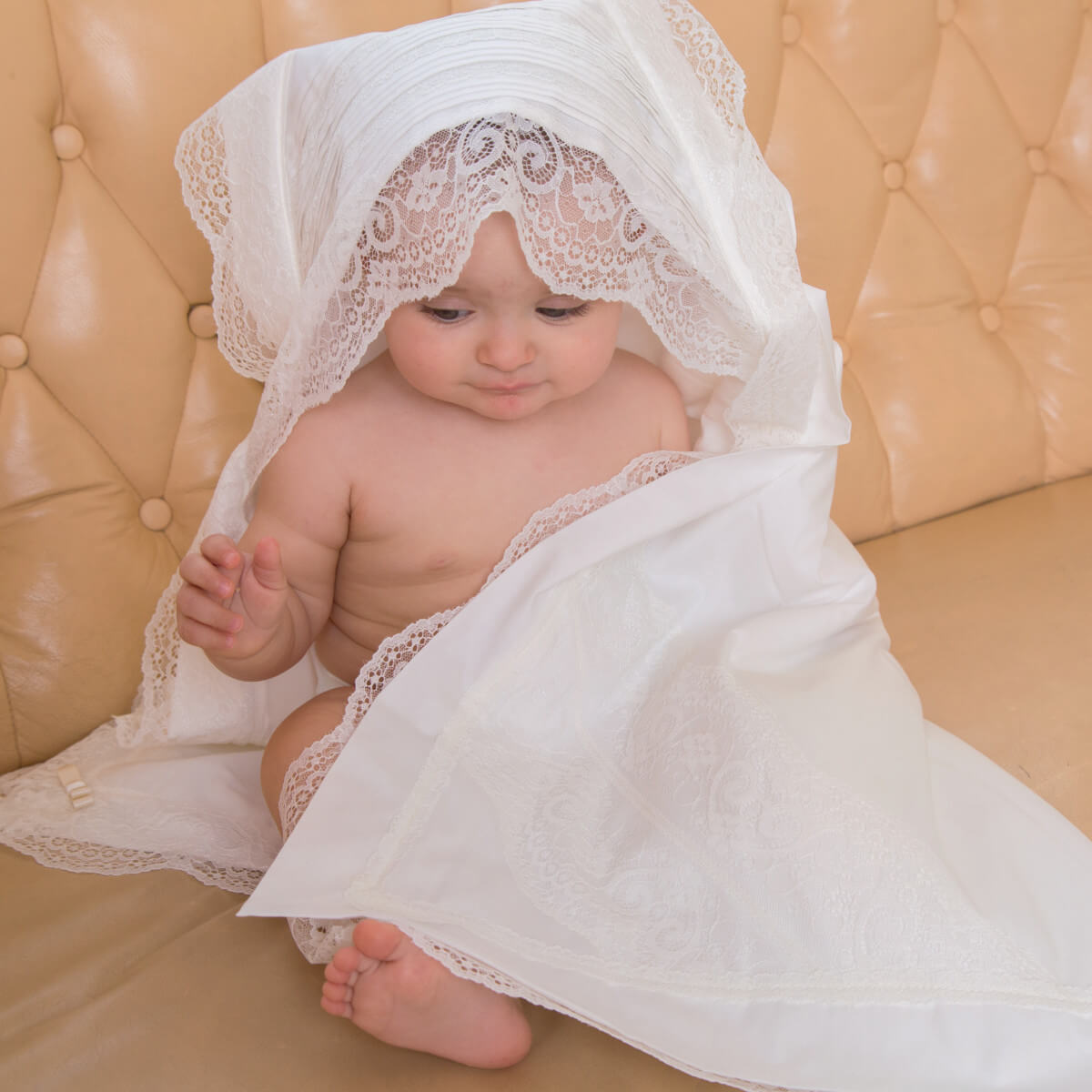Baby wrapped in a white lace blanket on a beige couch