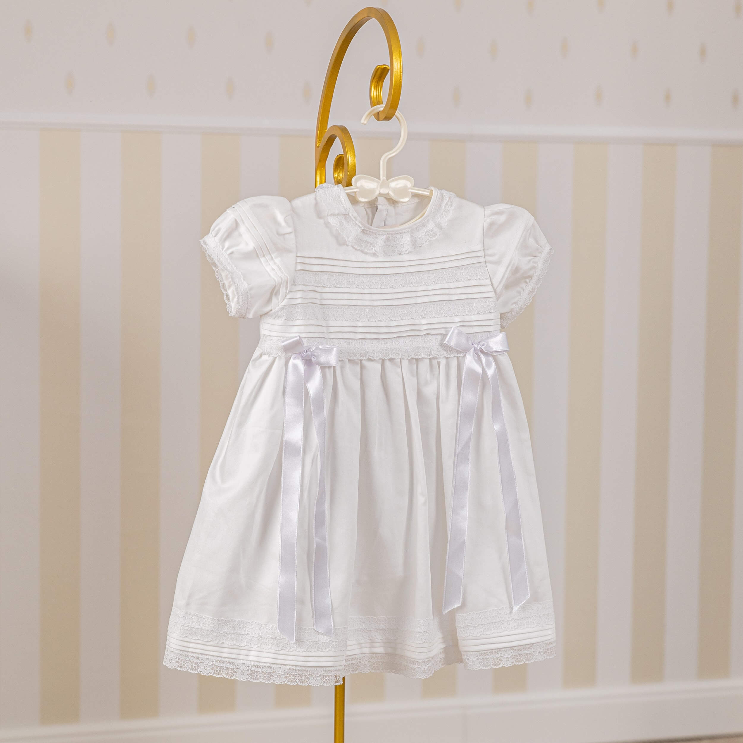 Cotton Christening Dress on a hanger against a striped wall