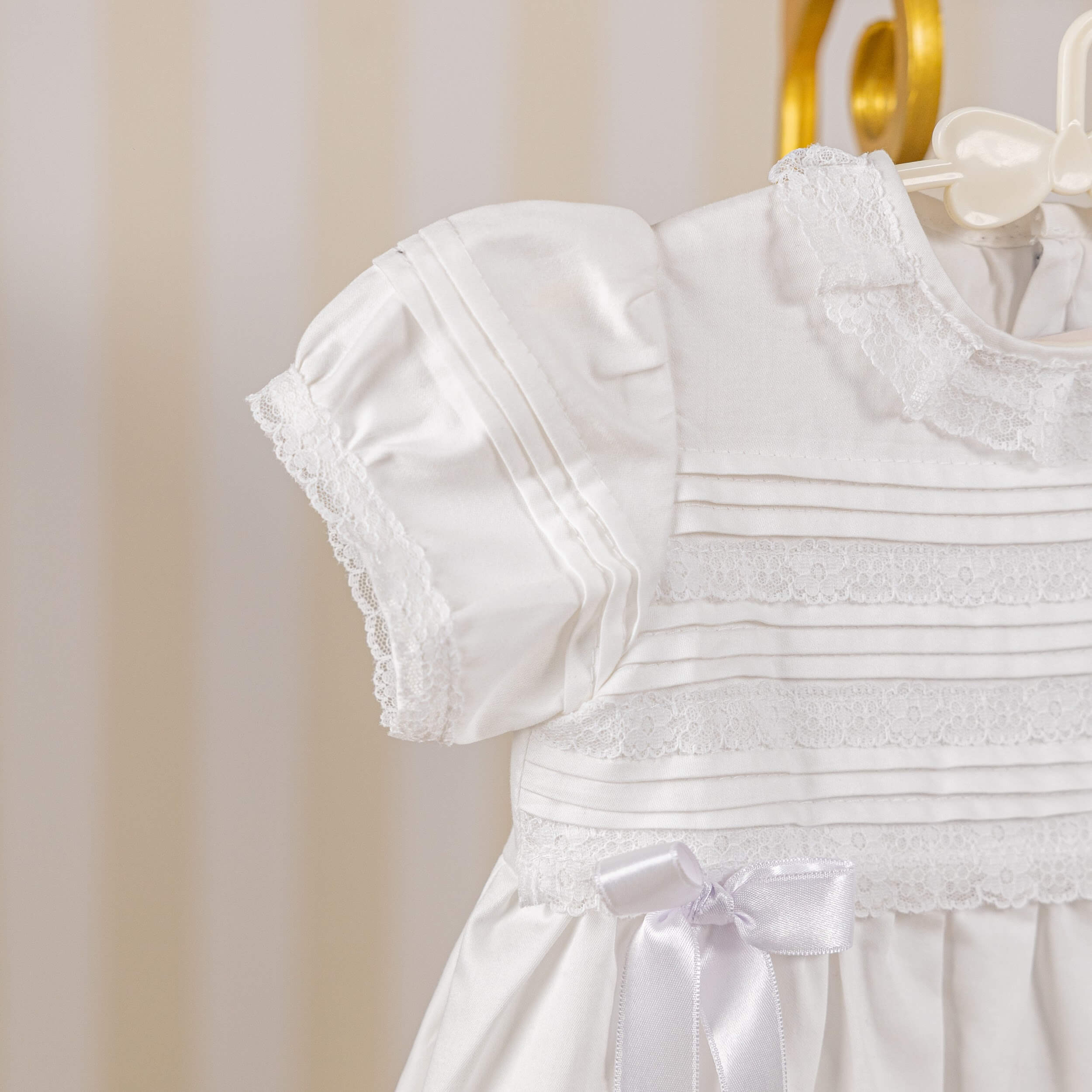 Cotton Christening Dress with a bow on a hanger against a neutral background