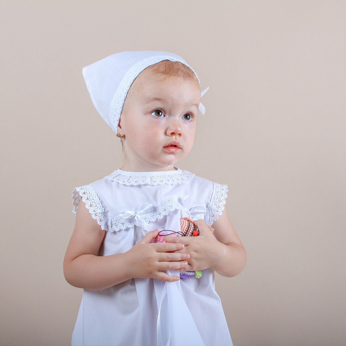 Young child wearing a Summer Baptism Dress Set for Girl with lace details and a matching headband against a beige background