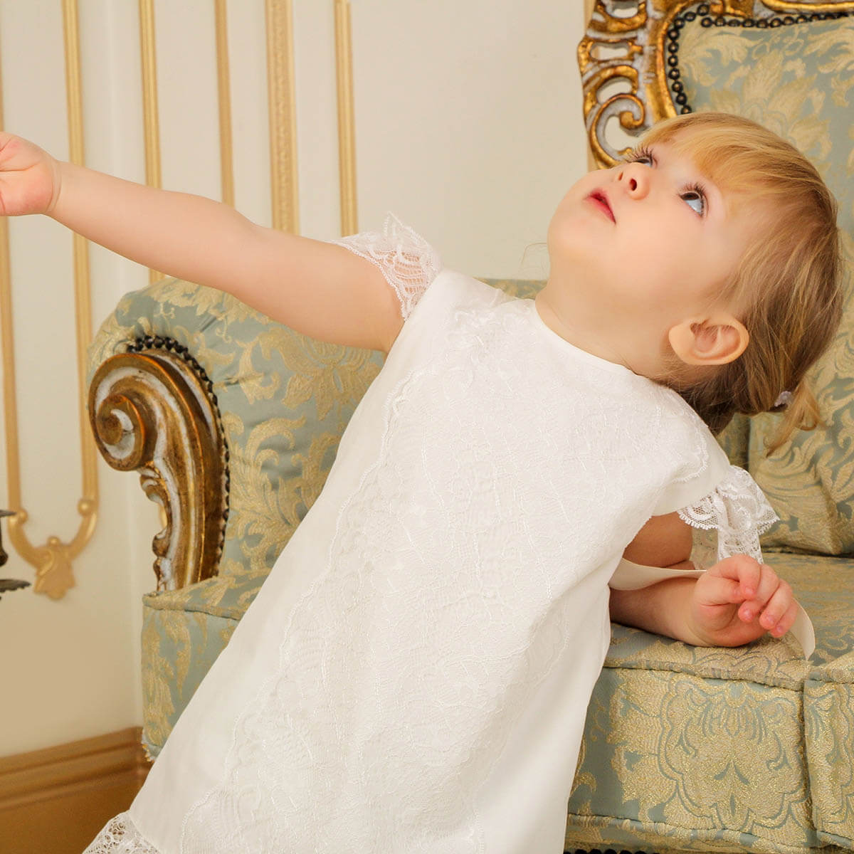 Child in a white baptism. dress sitting on an ornate chair