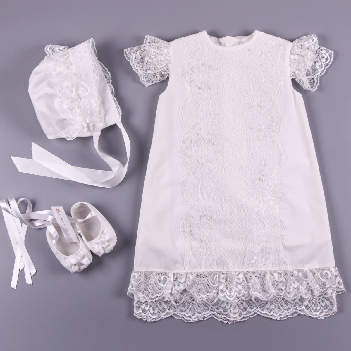 White lace baptism dress with matching bonnet, shoes, and ribbons on a gray background