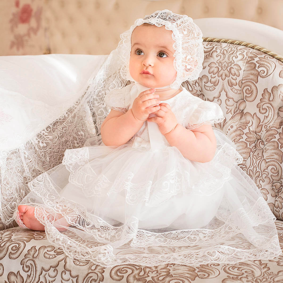 Baby in a Lace Baptism Bonnet sitting on an ornate couch