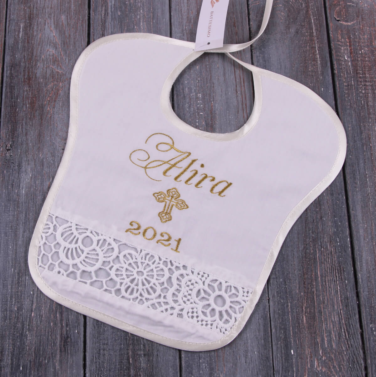 Baptism Bib with gold embroidery on a wooden surface