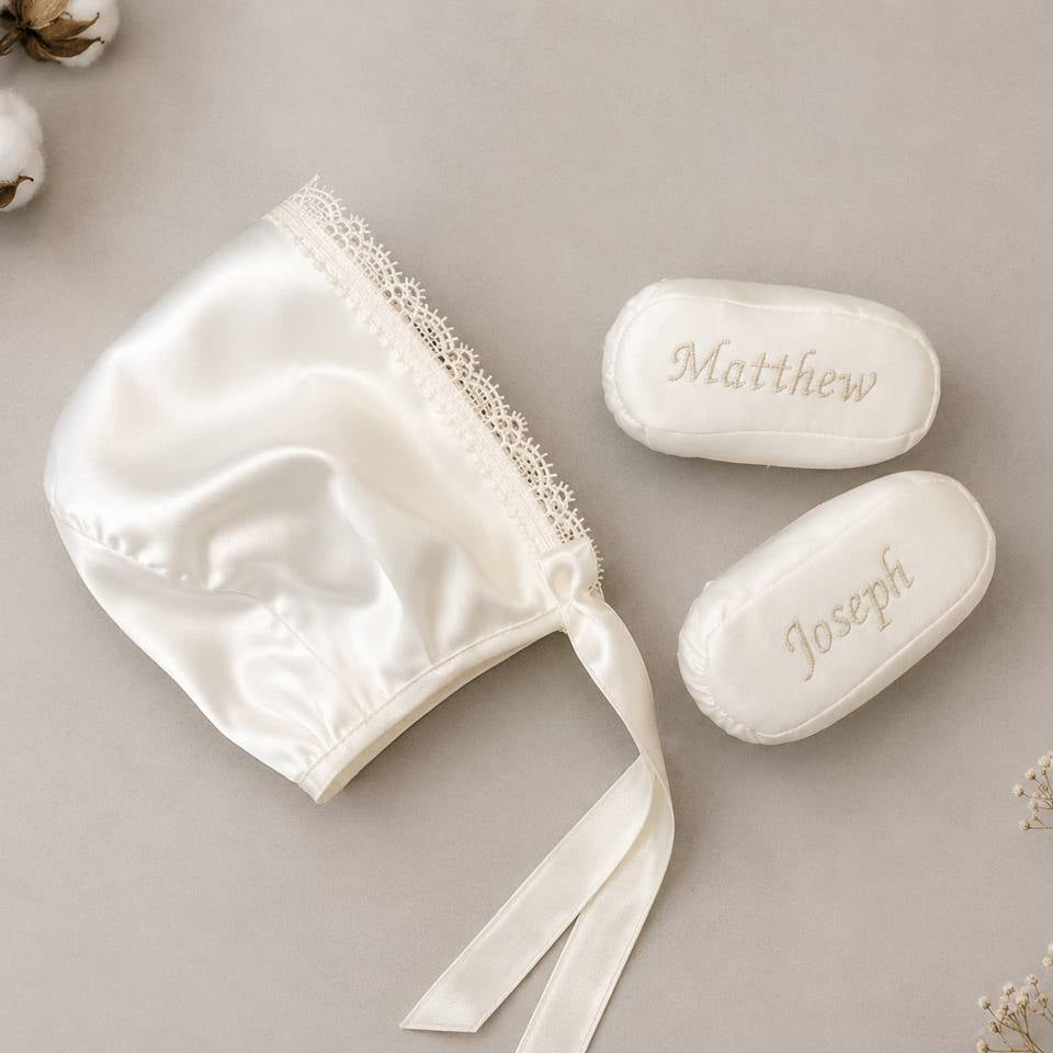 White baby bonnet with lace trim and personalized soap bars on a neutral background