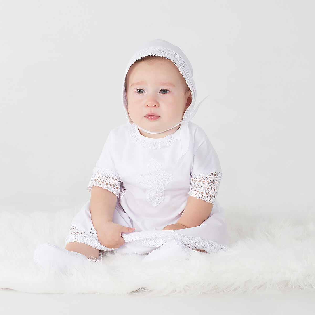 Baby wearing a Baptism Gown with lace details on a white background