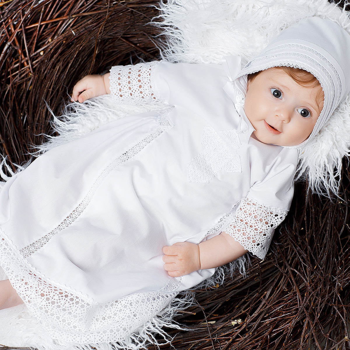 Baby dressed in a Baptism Gown with lace details, lying on straw.