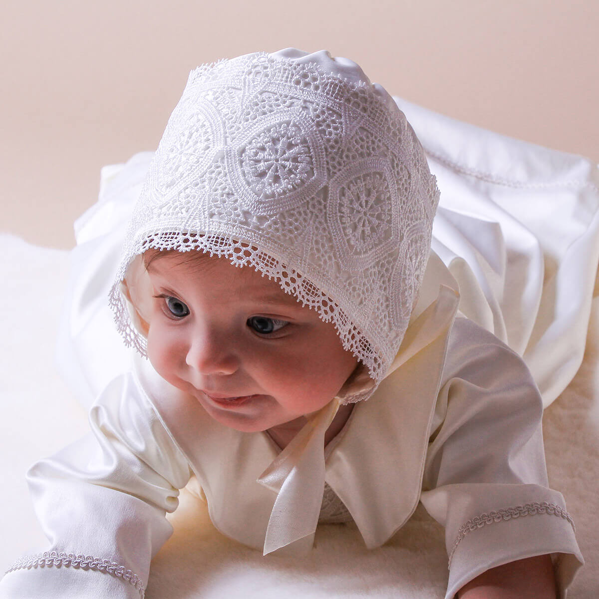 Baby wearing a white lace bonnet , as a part of Handmade Baptism Outfit on a light background
