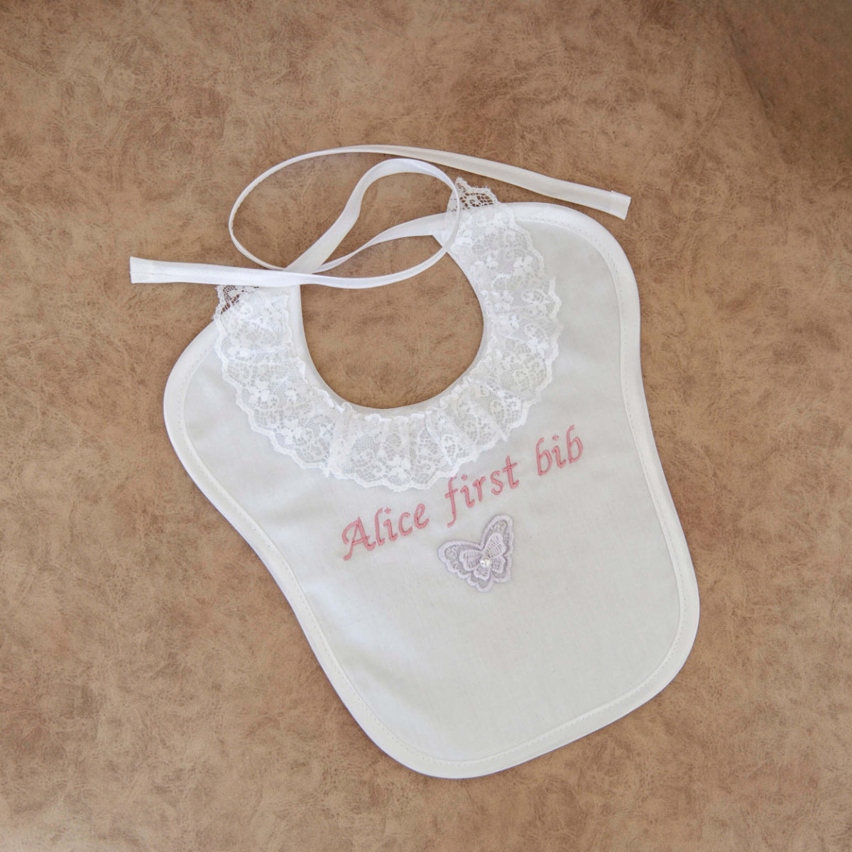 Baptism Bib with lace details and 'Alice first bib' text on a beige background