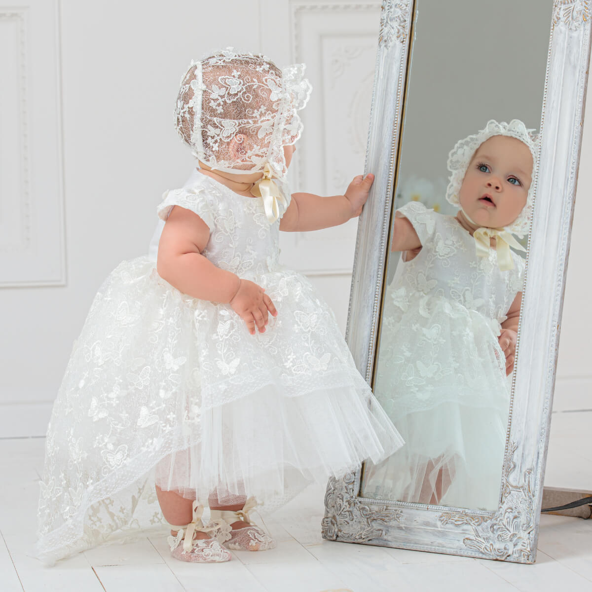 Baptism Dress with Lace and bonnet standing next to a mirror