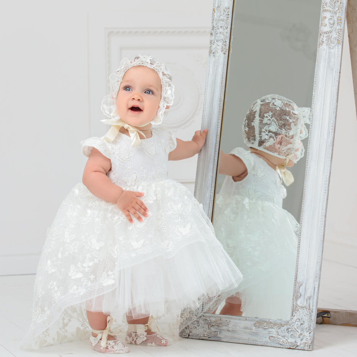 Baby in a Baptism Dress with Lace standing next to a mirror