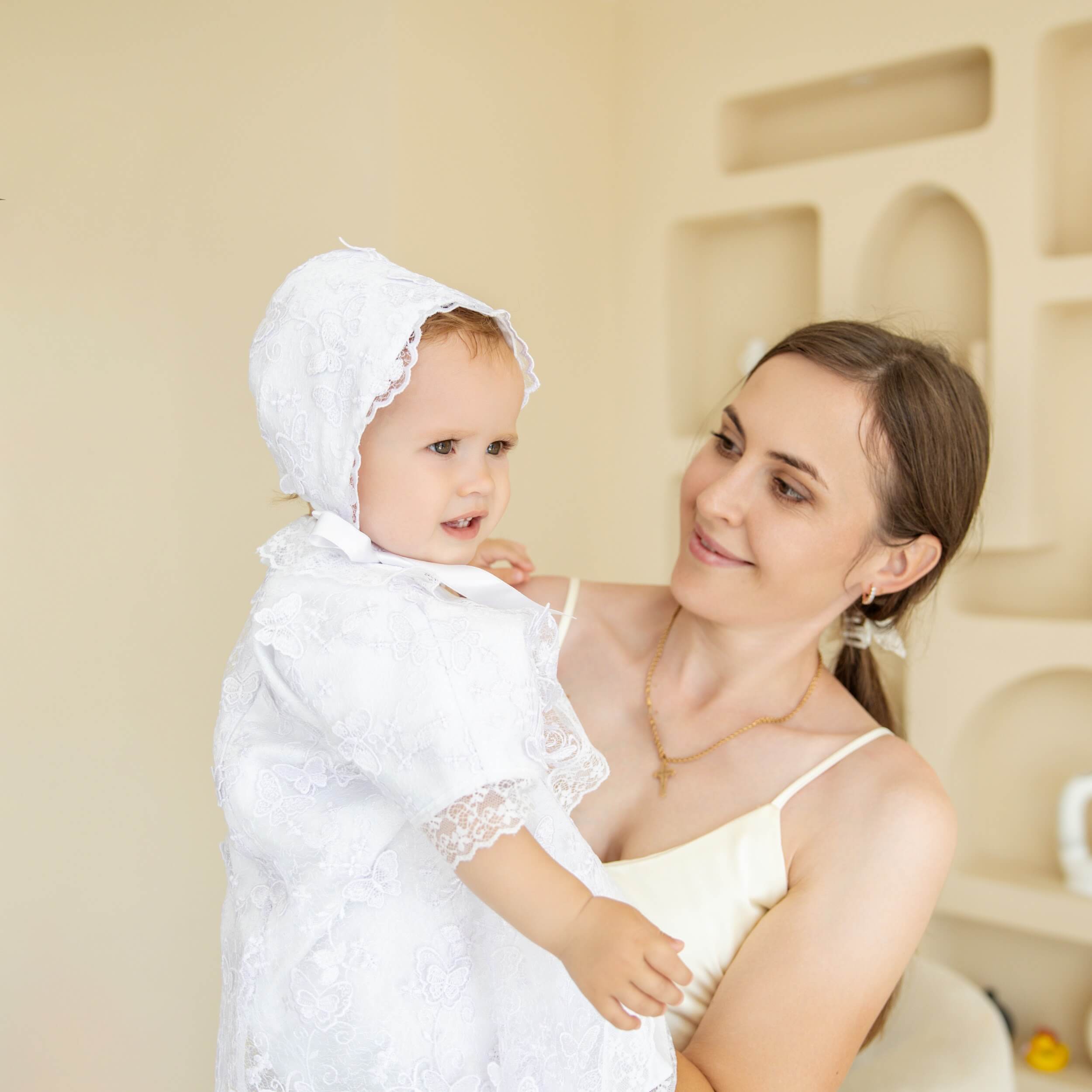 Woman holding a child dressed in  Christening Gown for Girls with a neutral background