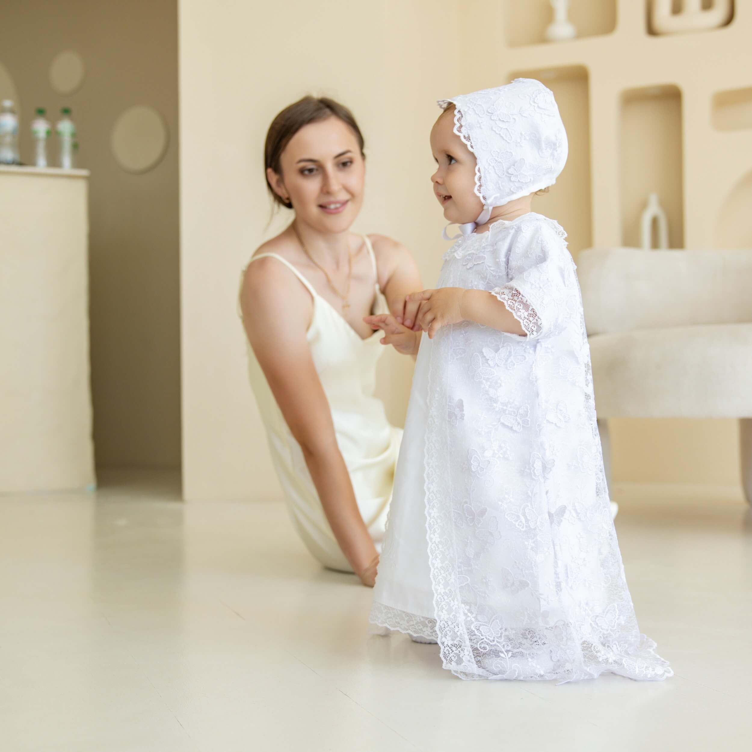 Woman and child in white l Christening Gown for Girls sitting together in a softly lit room.