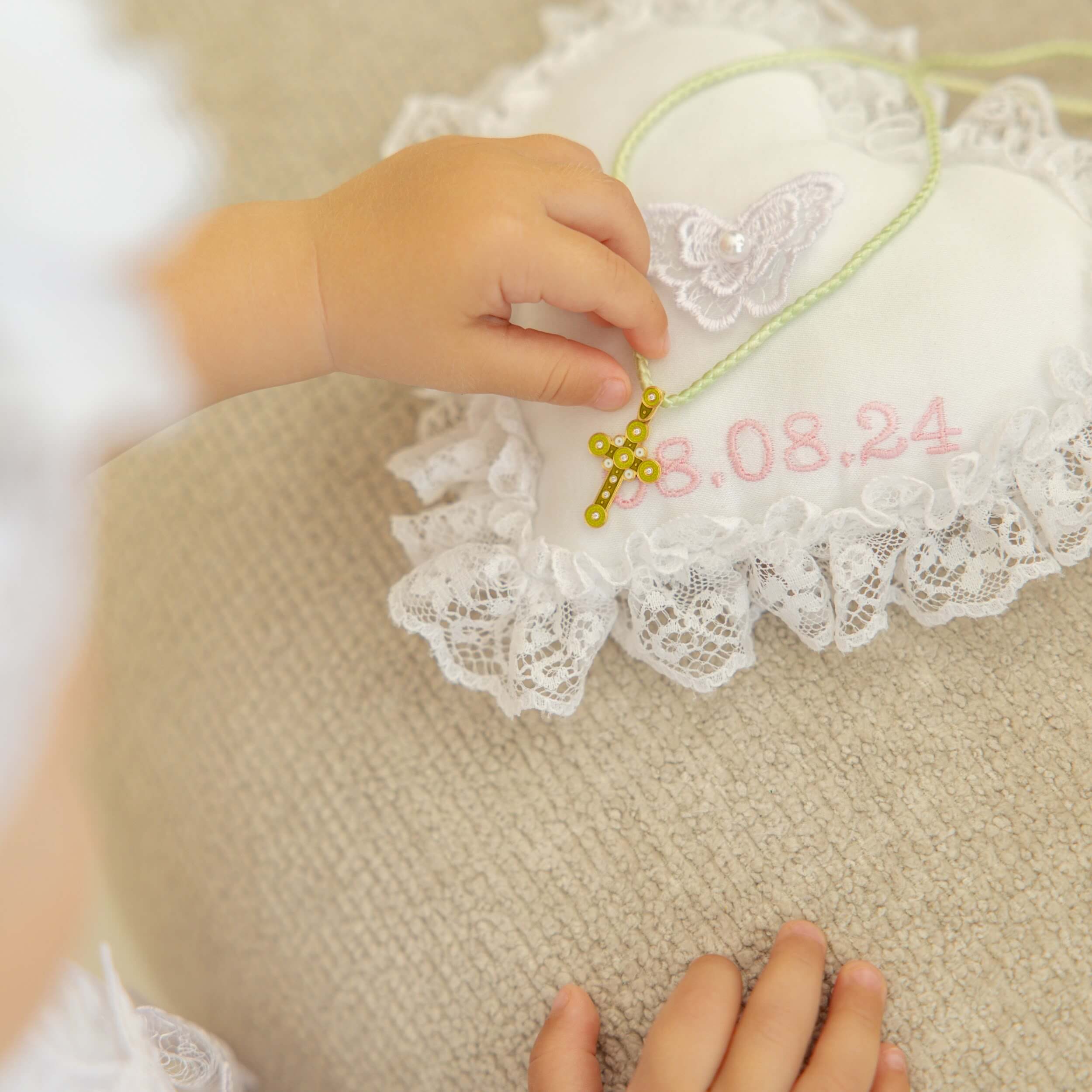 Child's hand holding a  Baptism Ring Pillow  with embroidered text on a textured surface.
