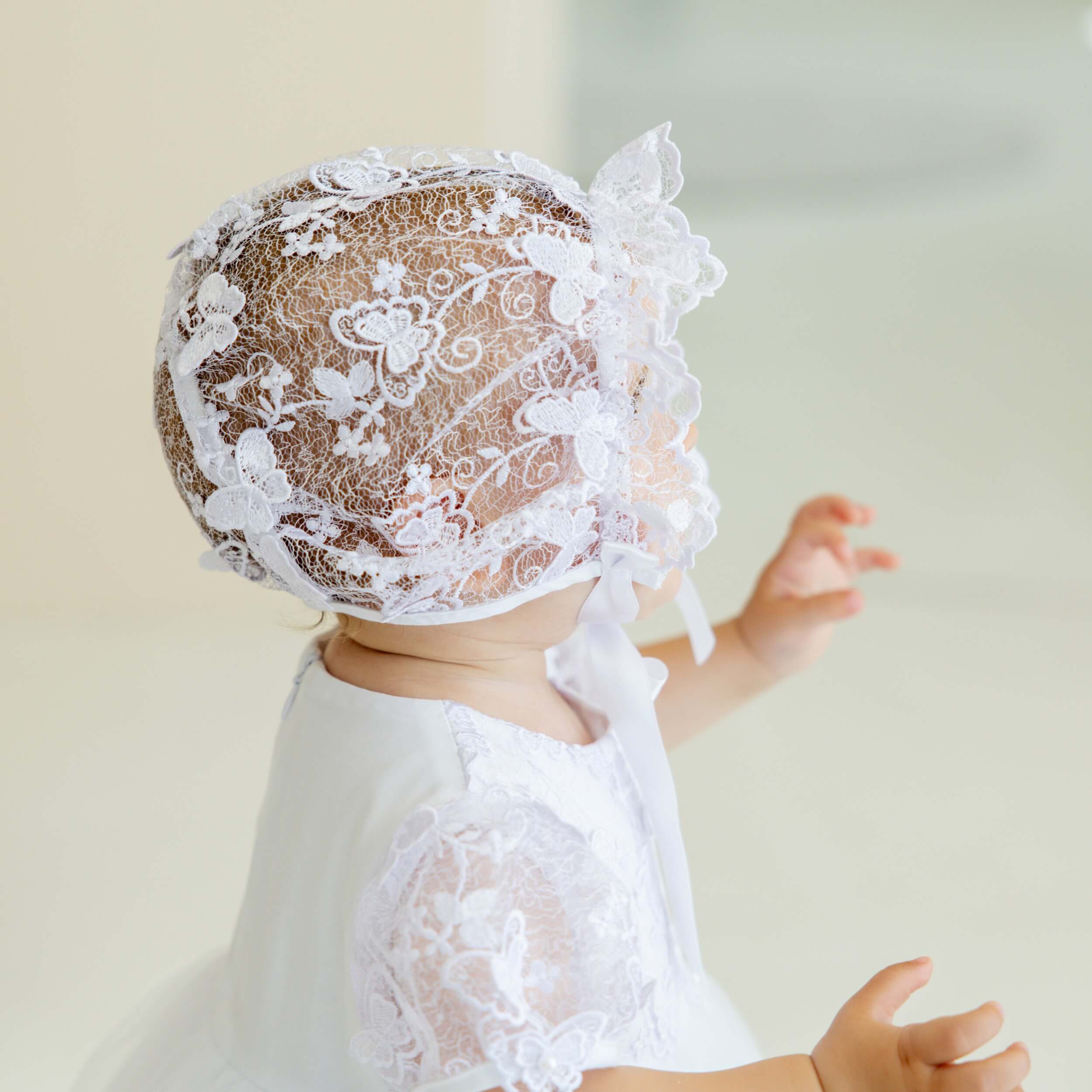 Baby wearing vintage baptism bonnet against a plain background