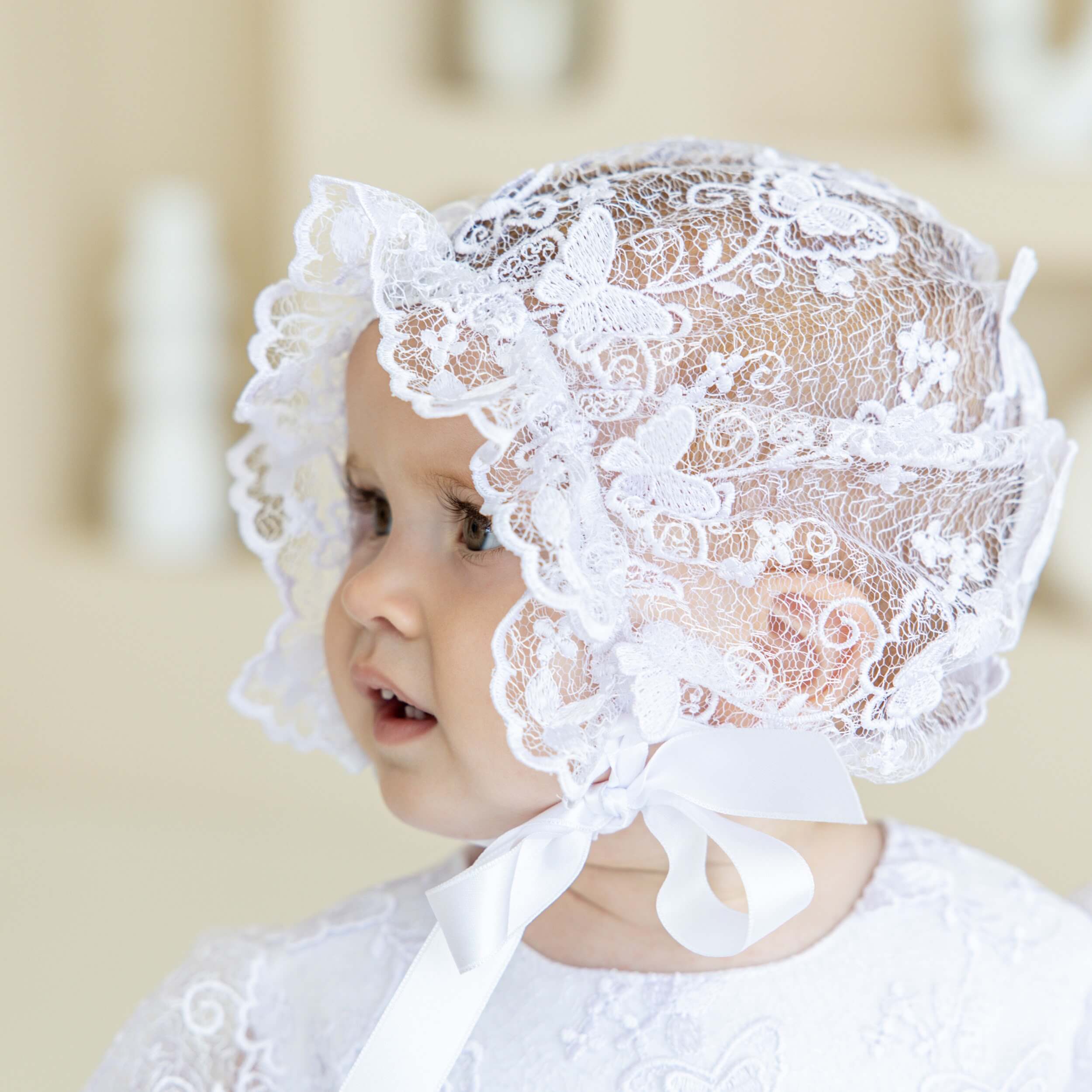 Baby wearing a vintage baptism bonnet against a neutral background