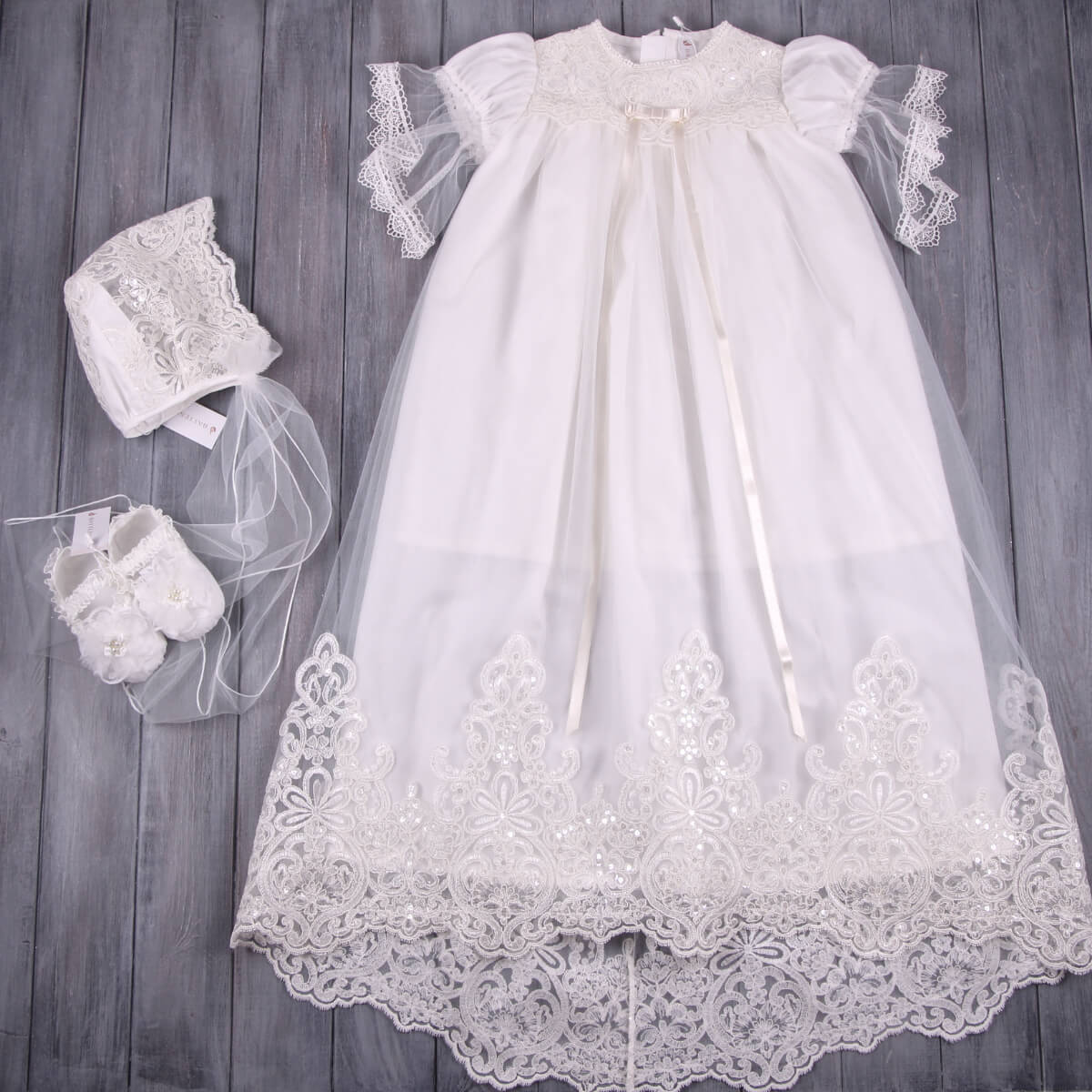Christening Gown with Train for Girls with matching bonnet and shoes on a wooden surface