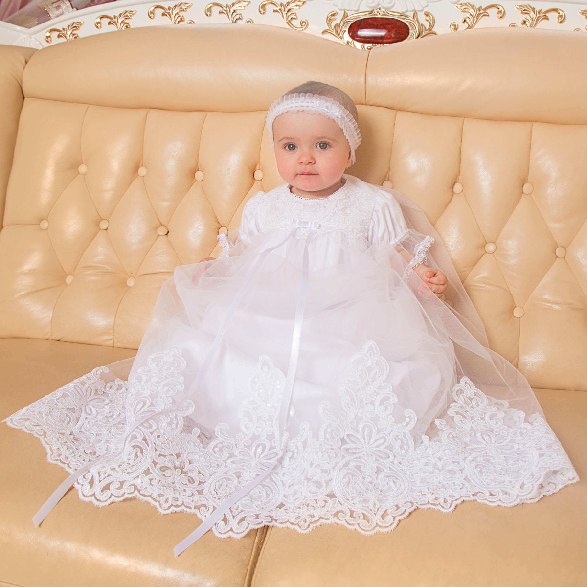 Baby in a Christening Gown with Train for Girls  sitting on a beige couch