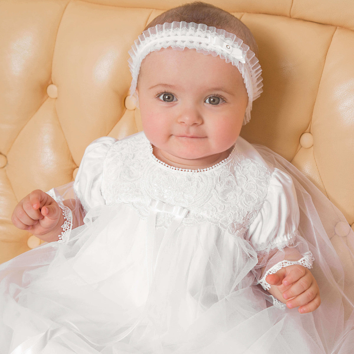 Baby in a Christening Gown with Train for Girls  sitting on a beige chair