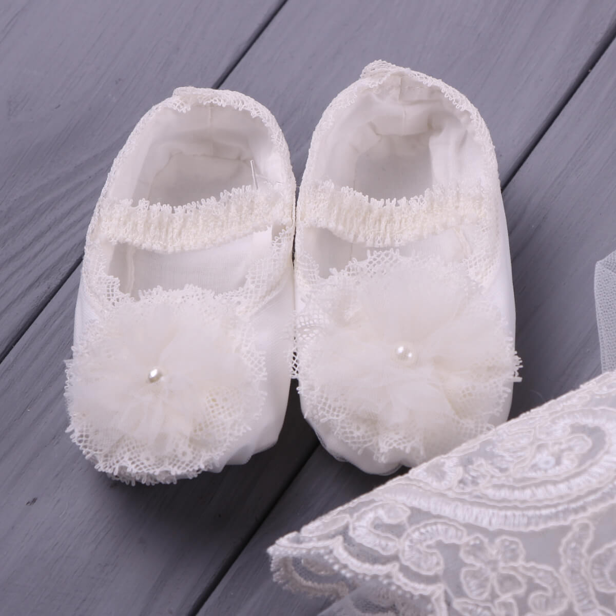 Pair of  Christening Booties with lace details on a wooden surface