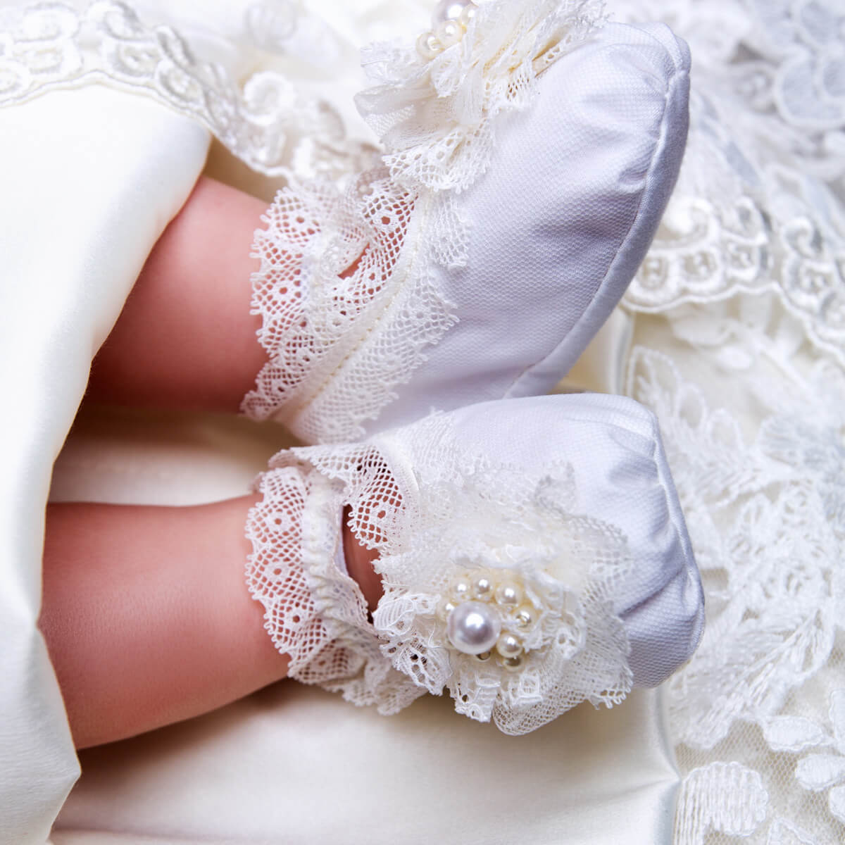 Christening Booties with a pearl embellishment on a white lace background