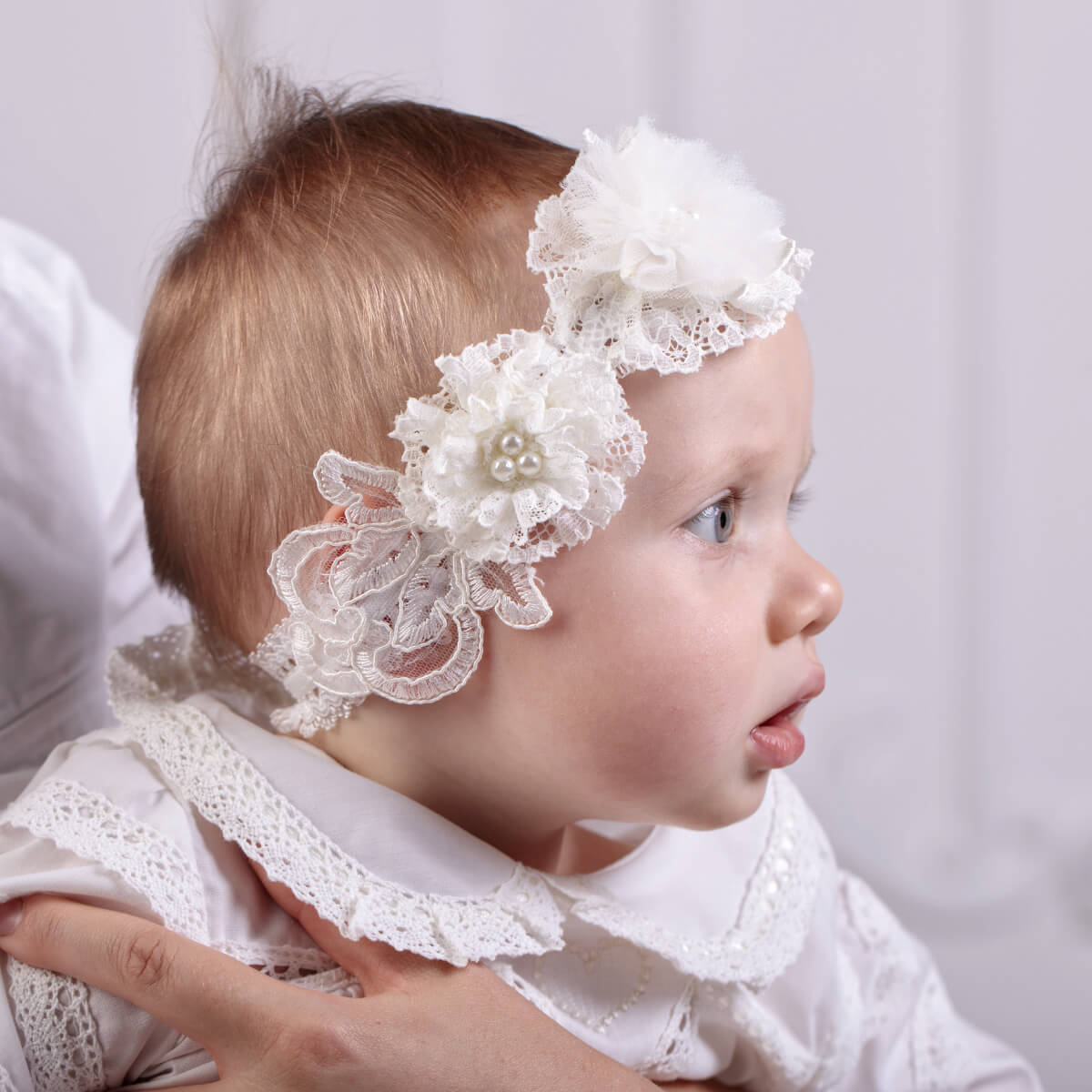 Child wearing a baby lace headband with floral details on a plain background