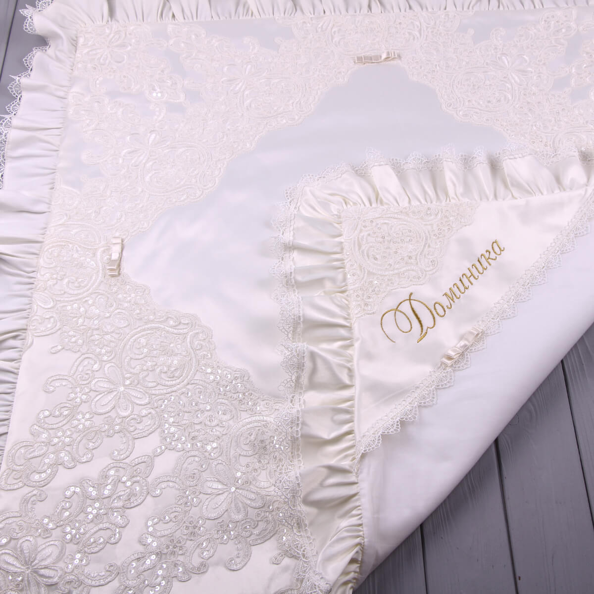 White embroidered christening blanket with gold text on a light wooden surface
