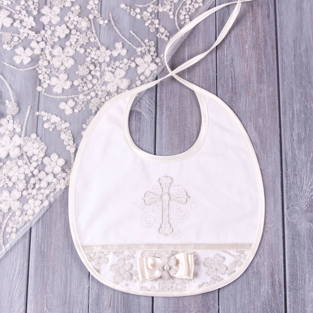 White baby bib with cross design on a wooden surface with floral decorations