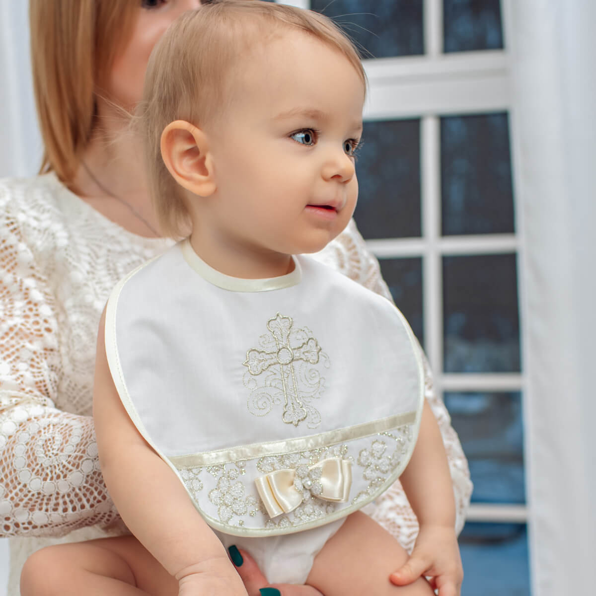 Baptism Bib with Delicate Lace with a cross design, sitting on a person's lap.