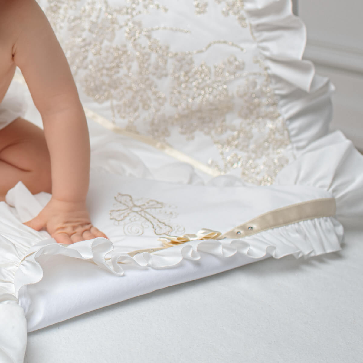 Baby in a white christening blanket with a cross design on a white background