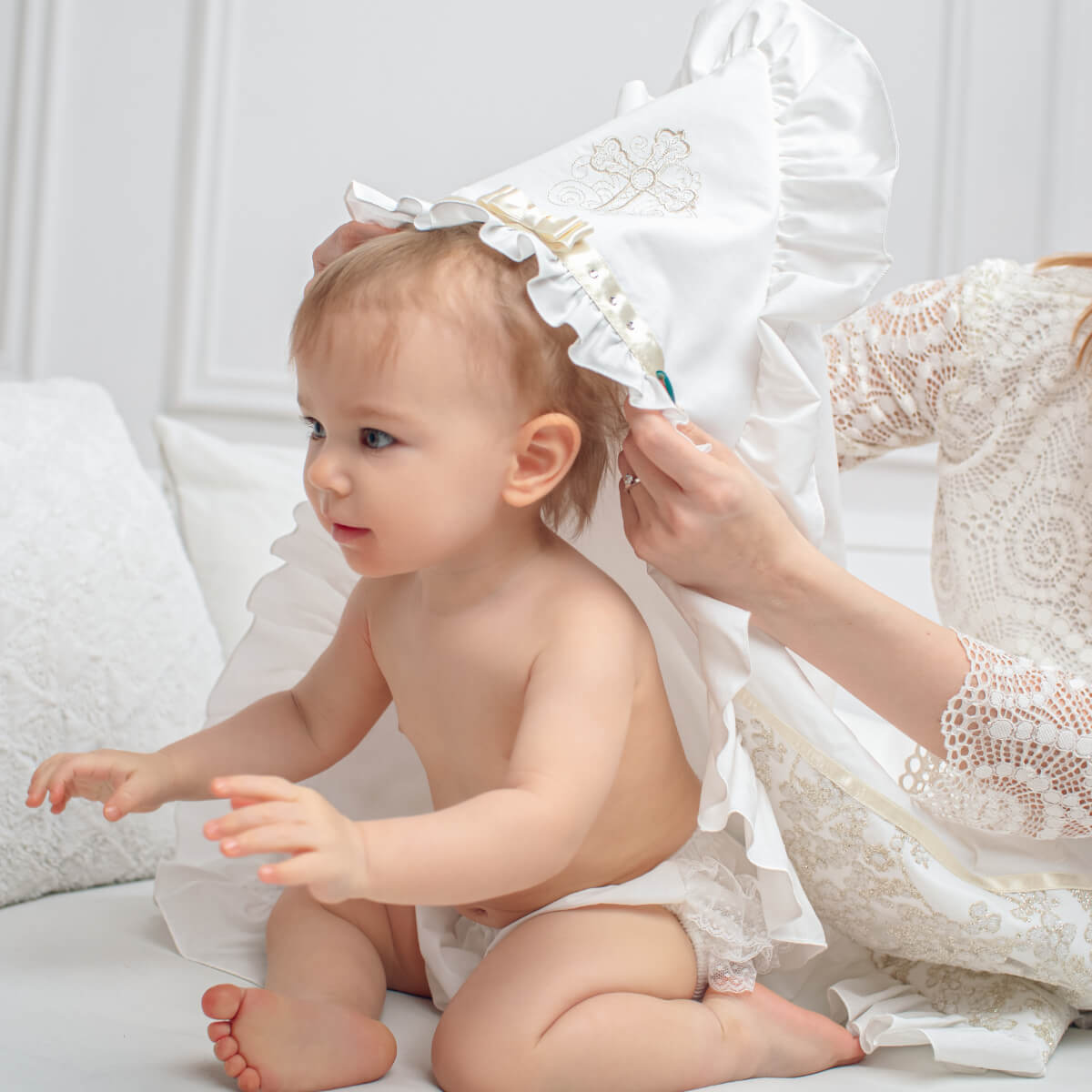 Baby being helped to put on a white lace christening blanket by an adult in a white dress.