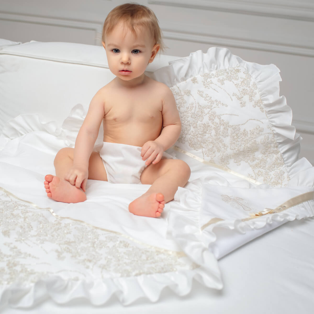 Baby sitting on a white christening blanket wearing a diaper.
