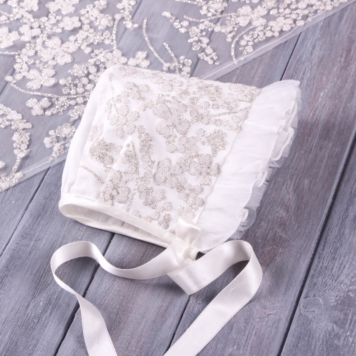 White Christening Bonnet with a ribbon on a wooden surface