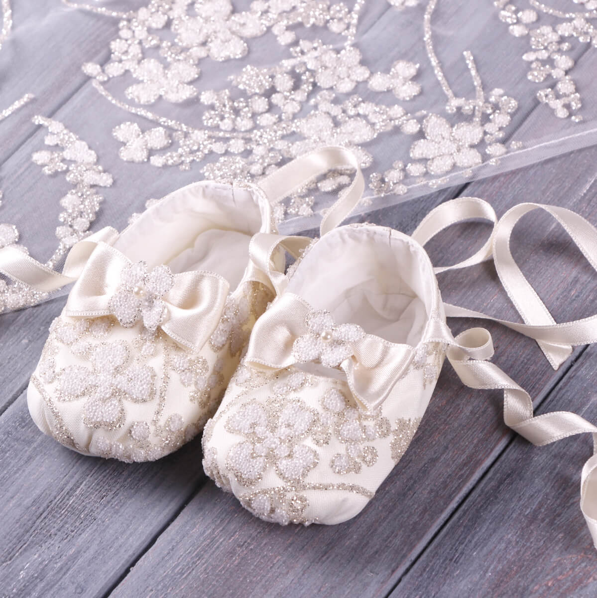 Pair of Christening Booties with lace details on a wooden surface.