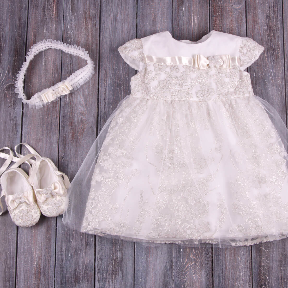 White lace dress with matching Christening Booties and headband on a wooden background