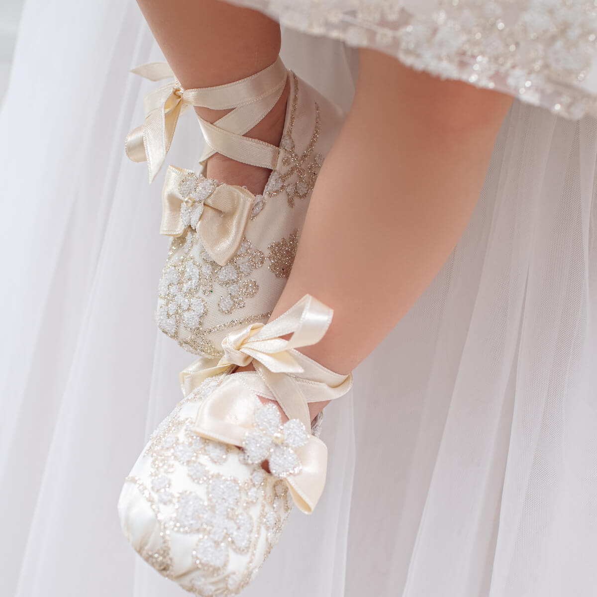 Christening Booties with ribbons and embellishments held by a person wearing a white dress.