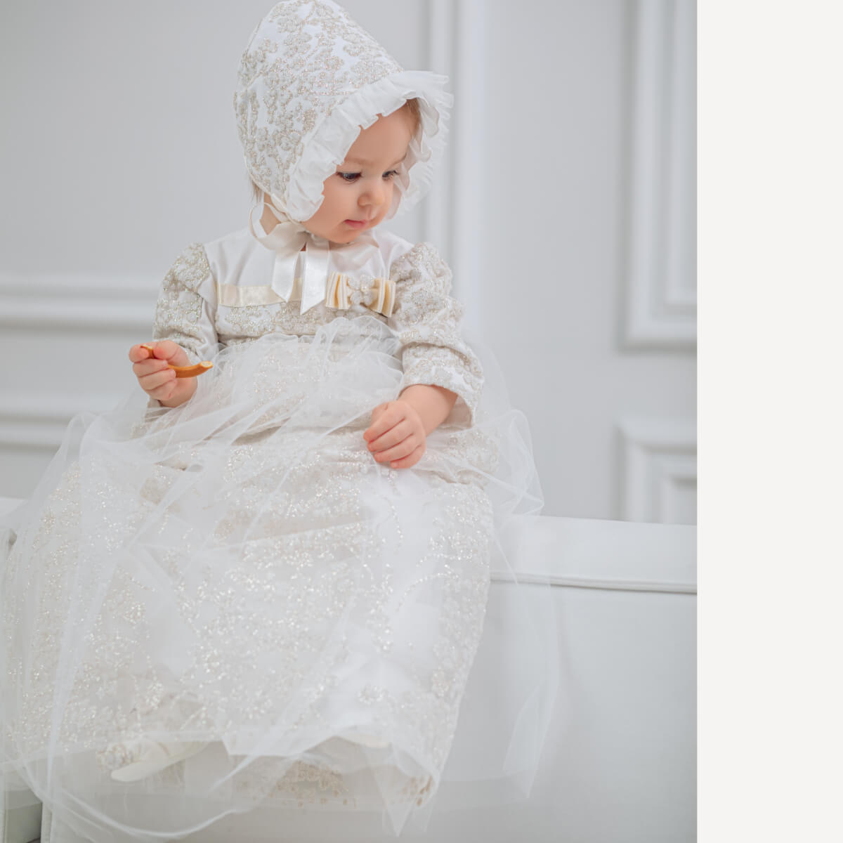 Baby in a  Christening Gown for Girls sitting on a white surface.