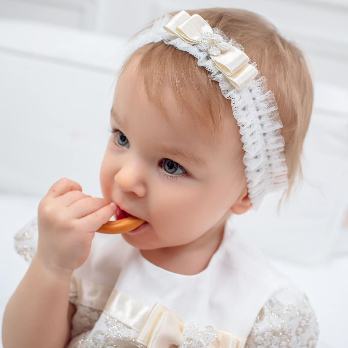 Girl wearing the baby  headband with a white bow, holding a teething ring.