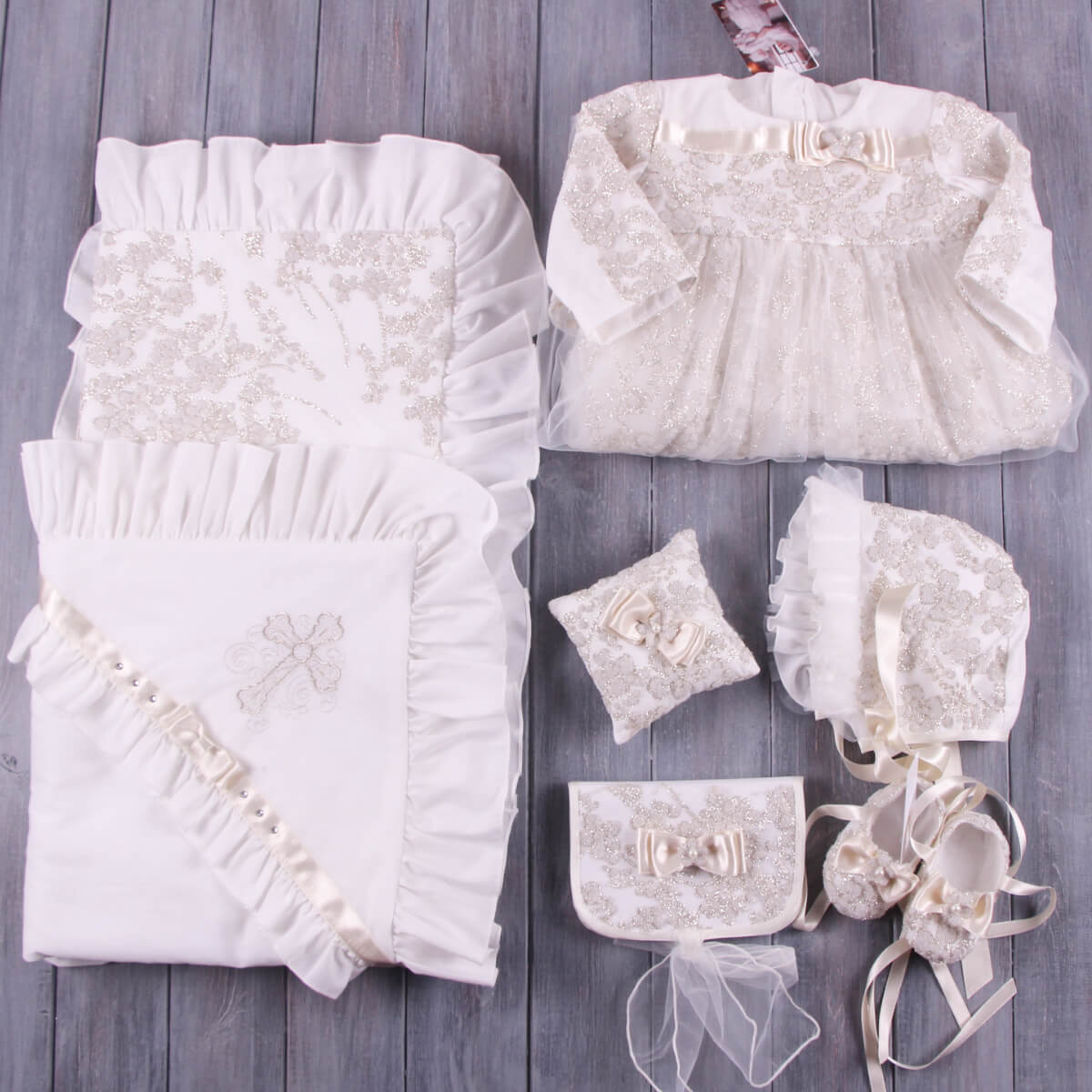 Collection of white lace baby clothing and Christening Ceremony Pillow on a wooden surface
