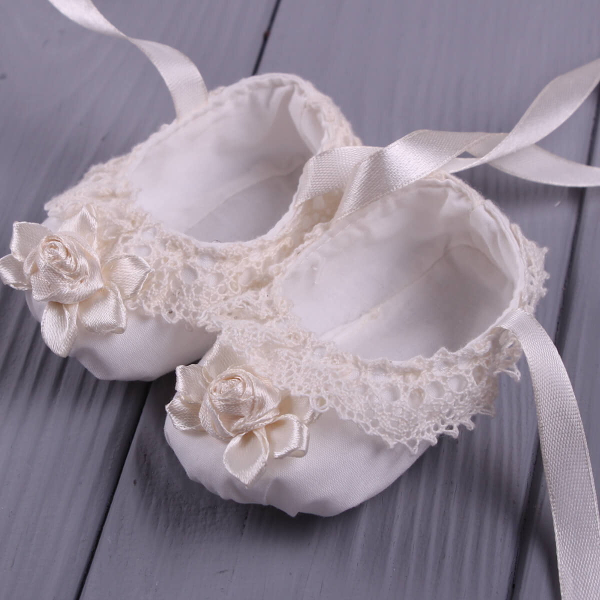 Christening Booties with lace and flowers on a wooden surface