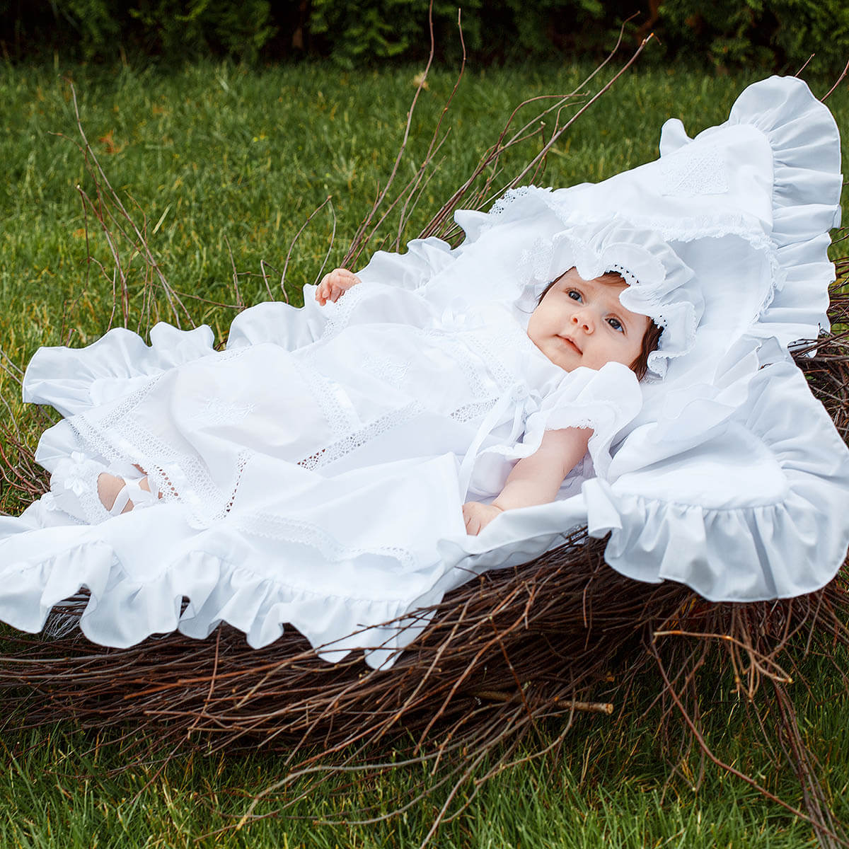 Baby in a white baptism blanket lying on grass