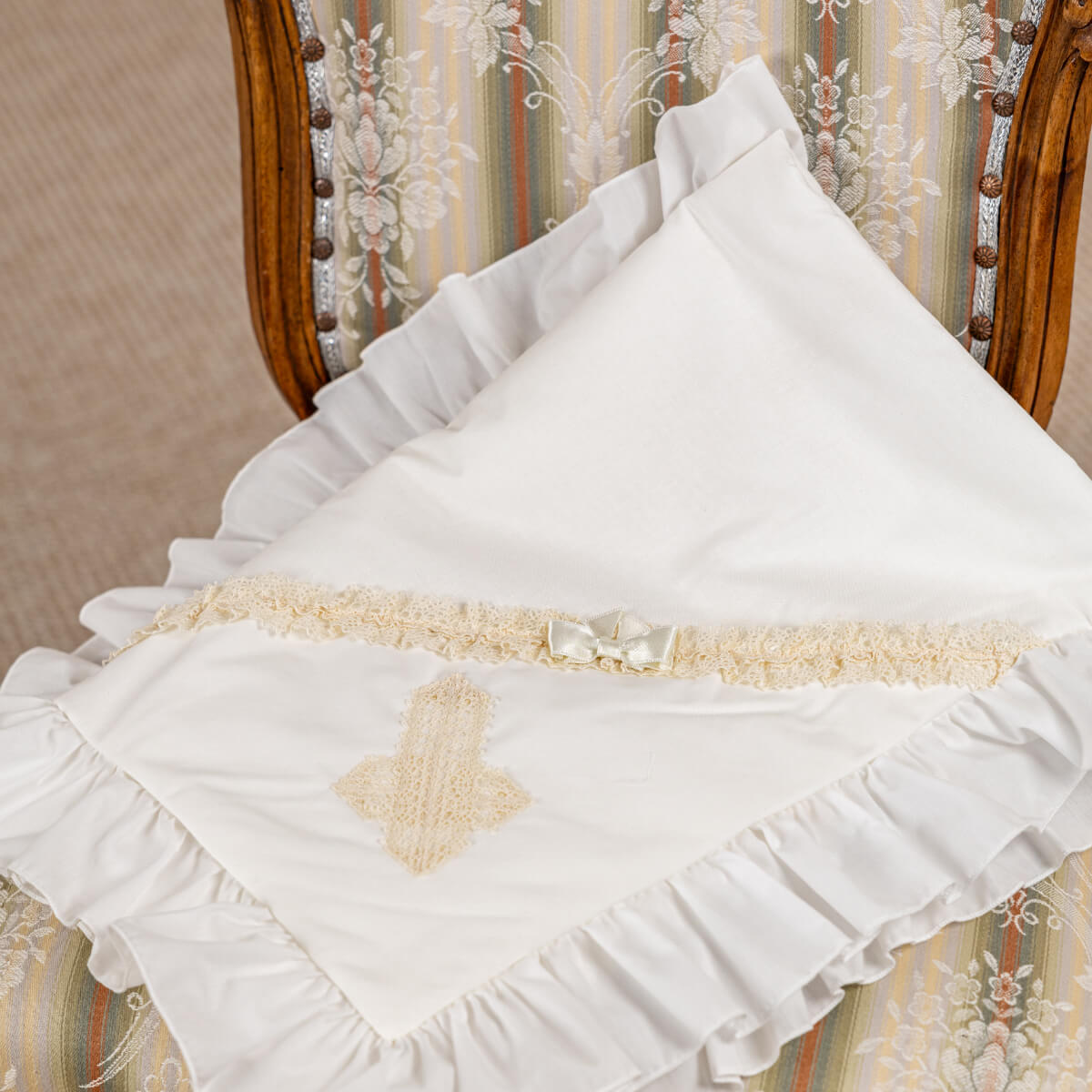 White baptism blanket with ruffles on a chair with floral patterned fabric.
