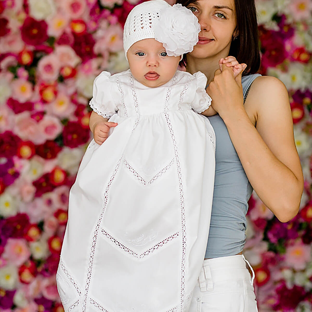Woman holding a baby dressed in a  Christening Gown for Girls against a floral background
