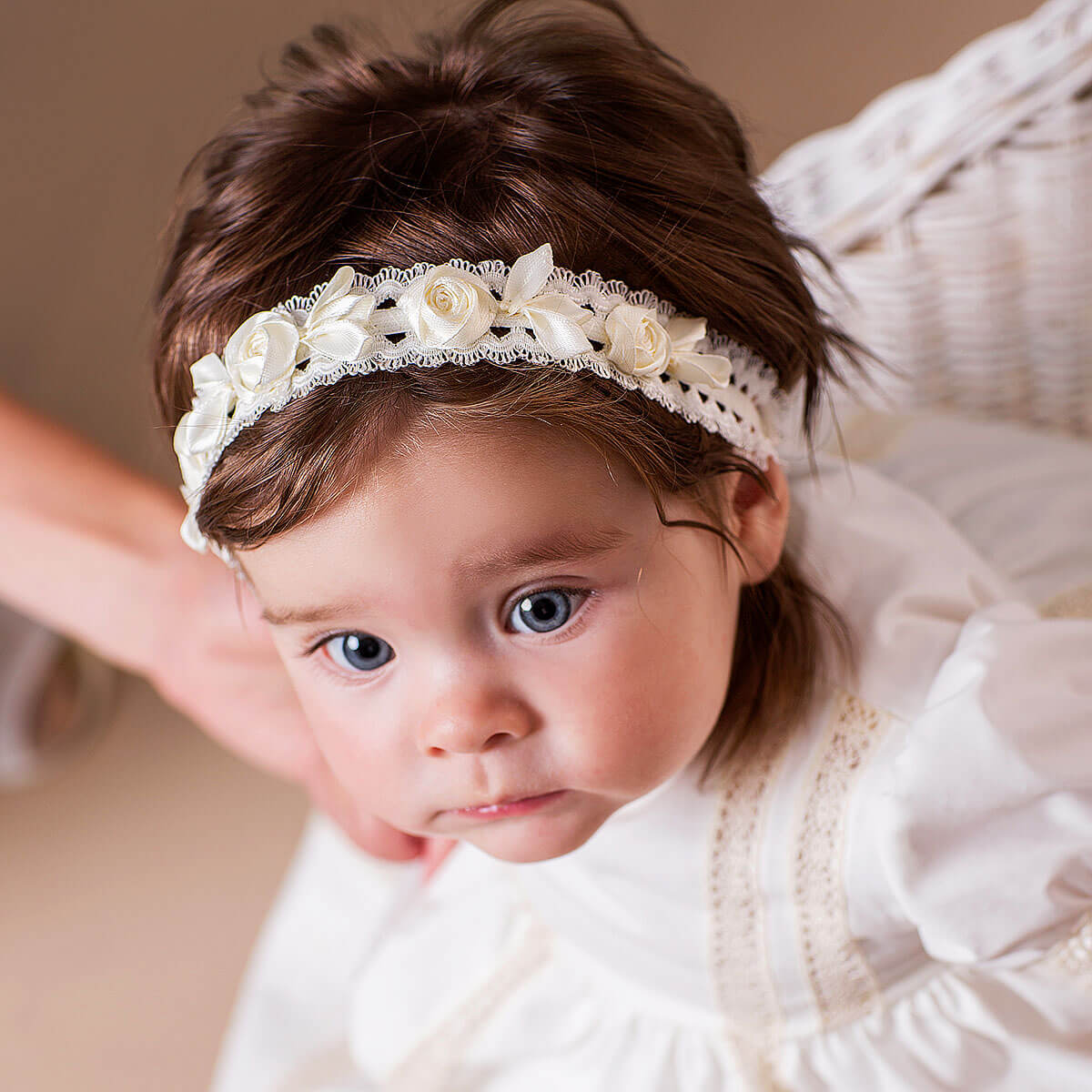 Baby  headband with white flowers and lace, against a neutral background.