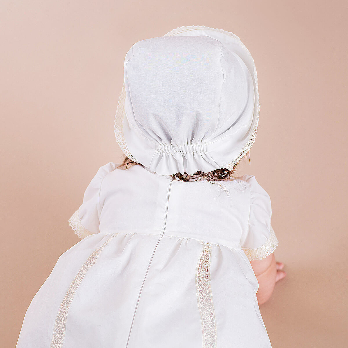 Child wearing a Baptism Bonnet and dress against a beige background