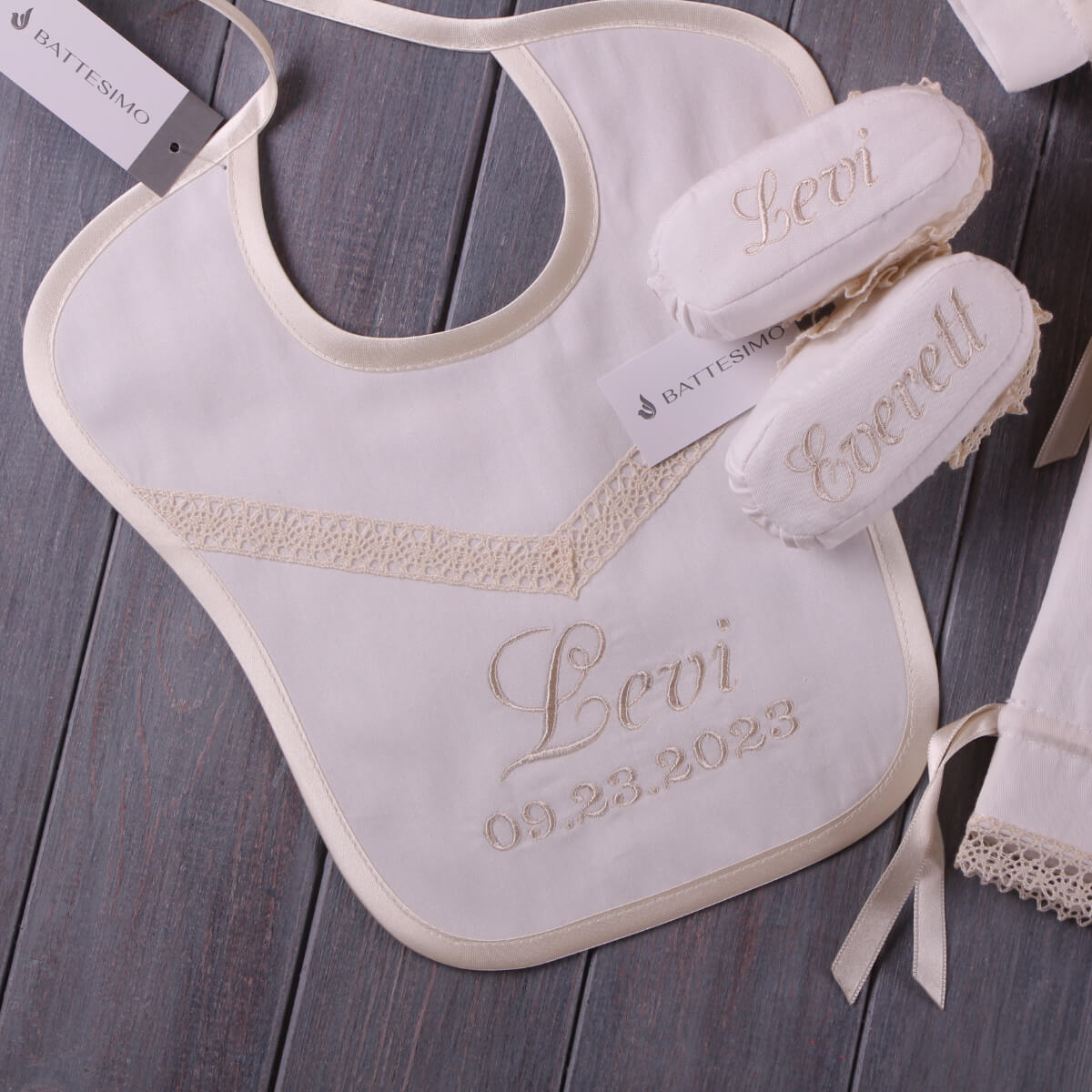 Baptismal set with Newborn Bib and booties on a wooden surface, featuring embroidered names and dates.