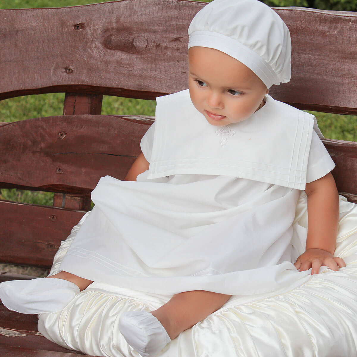 Baby in a christening outfitt sitting on a wooden bench outdoor