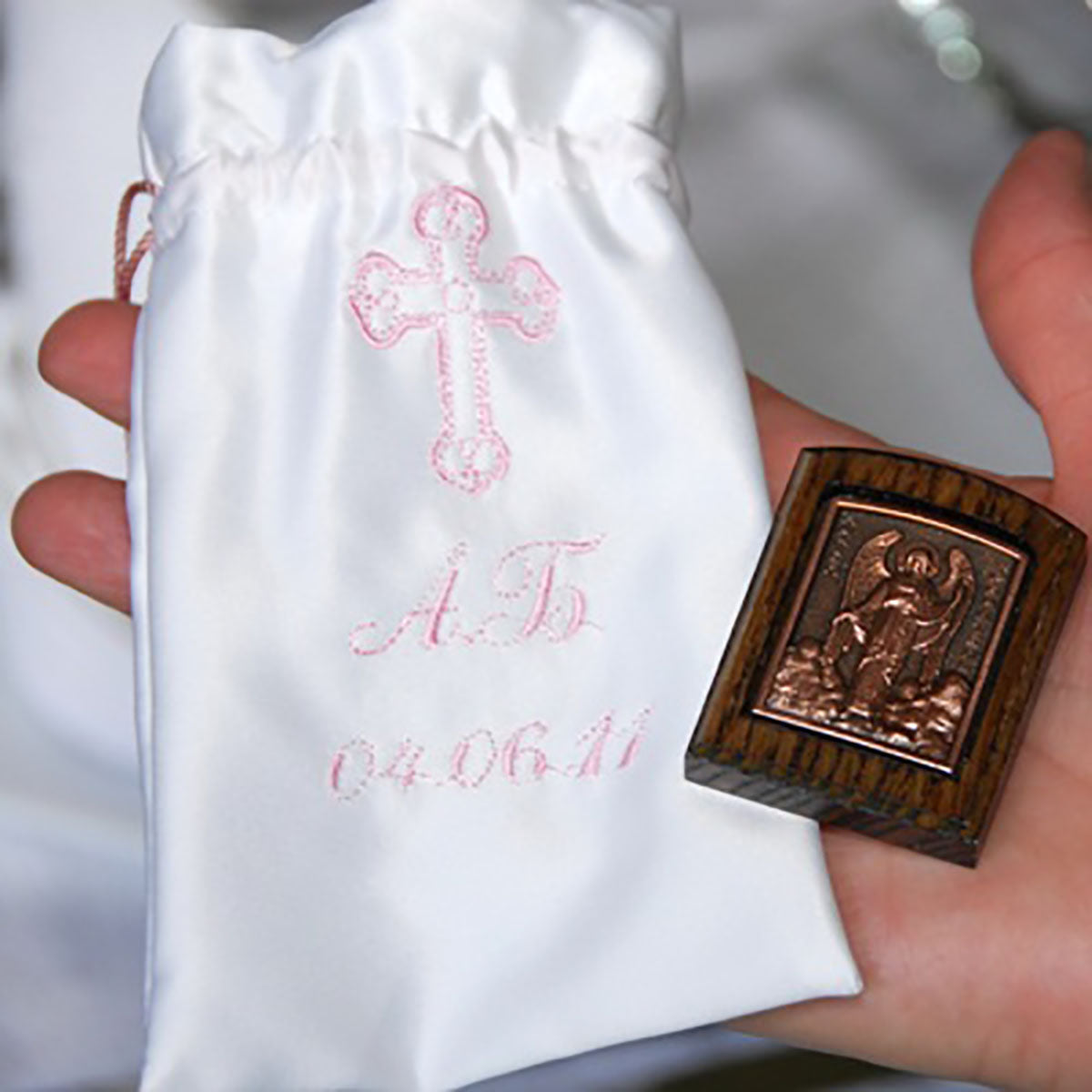 Baptism Keepsake Bonbonniere with red cross and text held by a hand, next to a wooden religious icon.